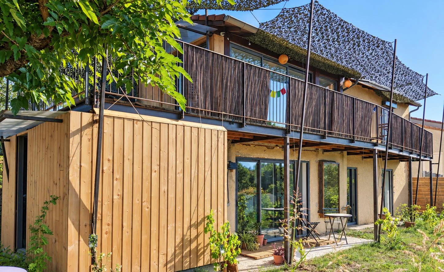 Le balcon en structure métallique, bois et canisses, au-dessus de la terrasse du rez-de-chaussée