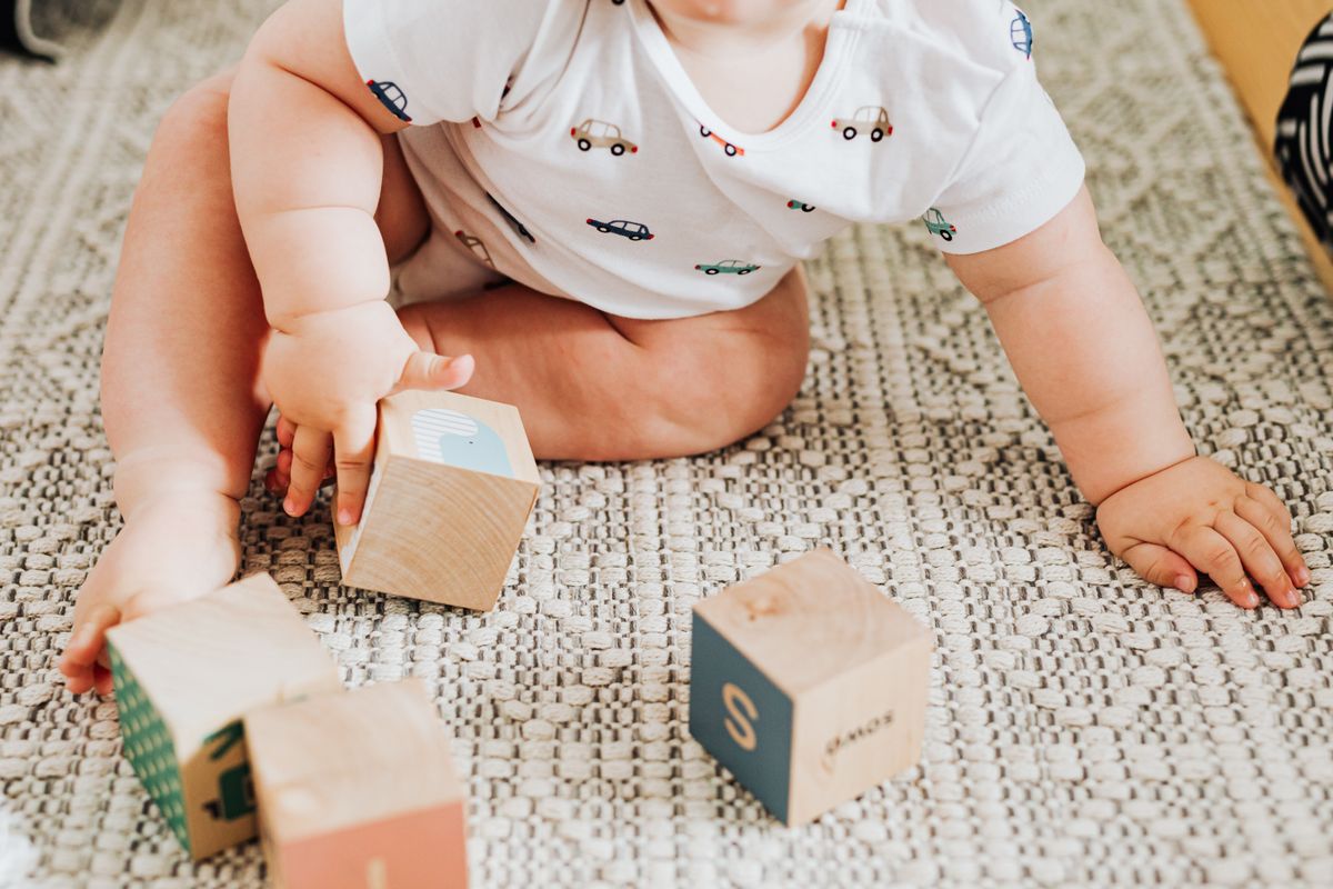 Un bébé assis sur un tapis attrape des cubes en bois, illustrant le développement de la motricité.
