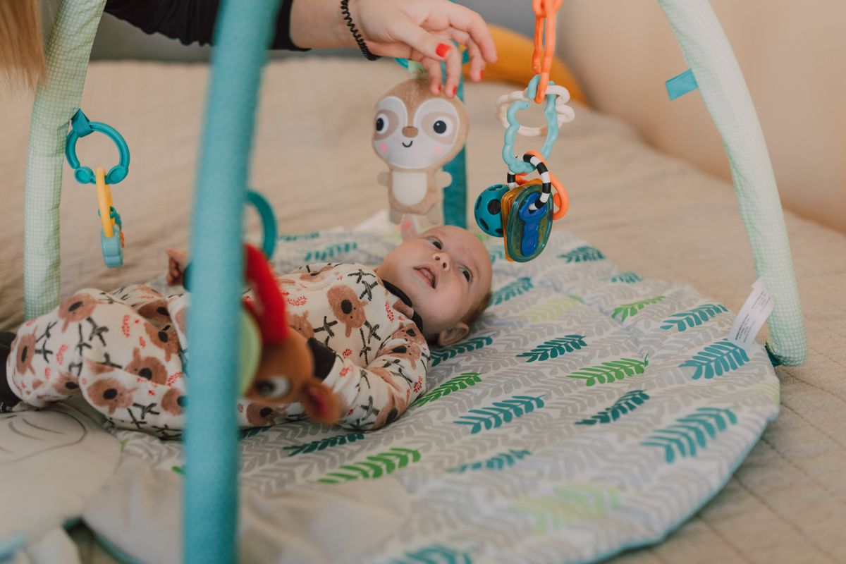 Un bébé allongé sur un tapis d’éveil observe des jouets suspendus.