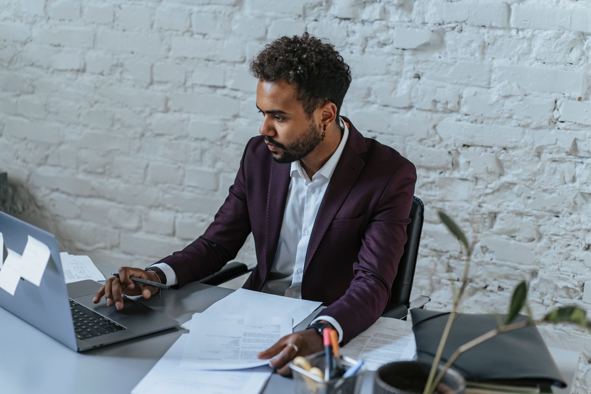 Un homme en tenue de bureau est assis à un bureau, en train de consulter un ordinateur portable et des papiers.