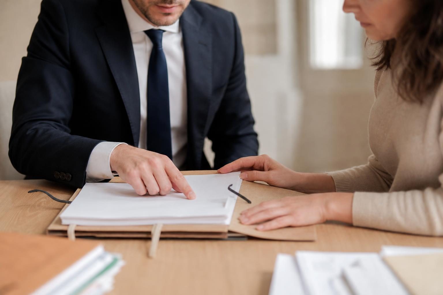Un homme en costume montre un dossier sur une table à une femme assise en face de lui dans un bureau sobre.